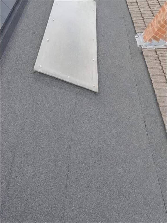 A finished felt flat roof, with a lead saddle dressed into the brickwork at the abutment