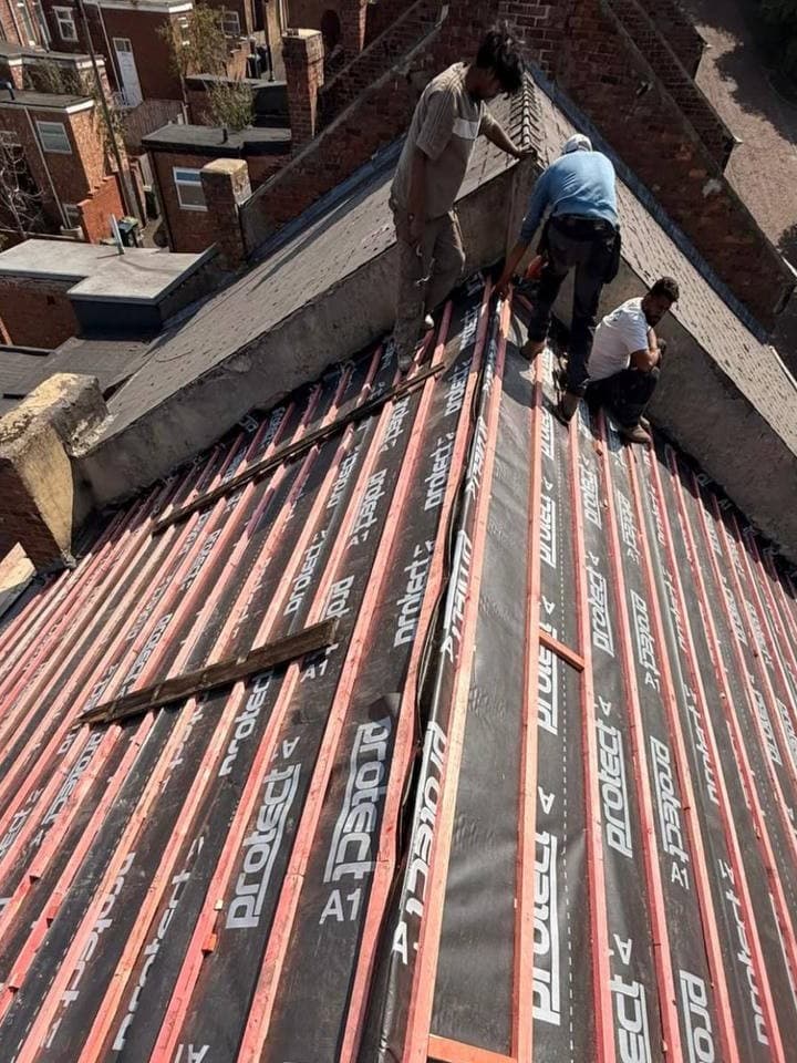 Three roofers working at the ridge of a large reroof, with membrane and battens laid out below them