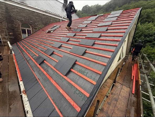 New slates being laid in courses over membrane and treated battens on a stone building